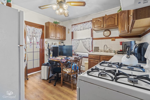 kitchen with white appliances, brown cabinets, a sink, and light wood-style flooring