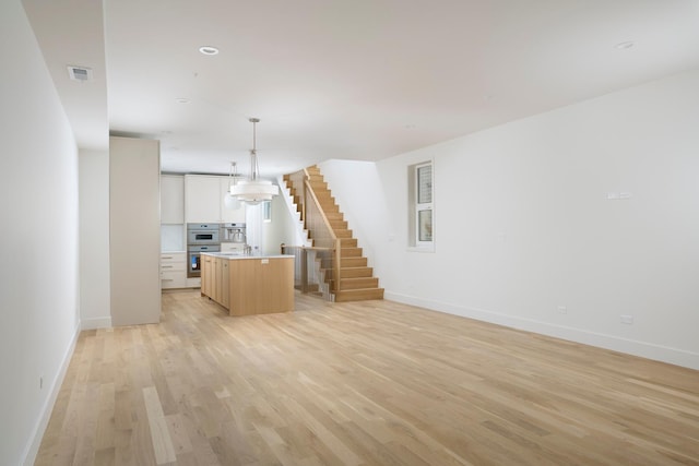 unfurnished living room featuring baseboards, stairs, light wood finished floors, and visible vents