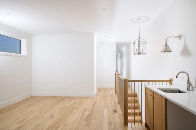 kitchen with brown cabinetry, decorative light fixtures, light wood-type flooring, a sink, and baseboards