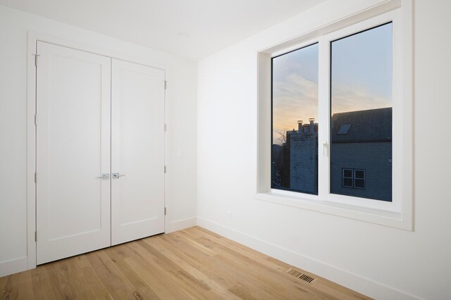 unfurnished bedroom with baseboards, wood finished floors, visible vents, and a closet