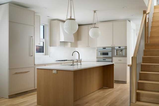kitchen featuring decorative light fixtures, a sink, light countertops, light wood-style flooring, and an island with sink