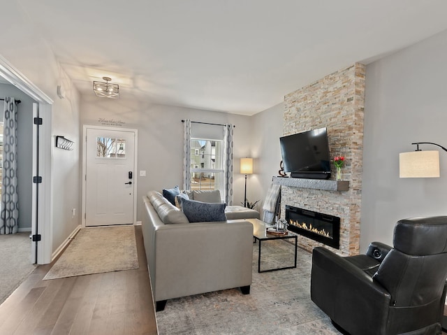 living room featuring a stone fireplace, baseboards, and wood finished floors