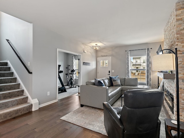 living room with a stone fireplace, stairway, baseboards, and wood finished floors