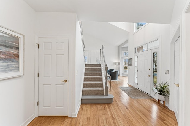 entryway with lofted ceiling, light wood-style floors, stairs, and baseboards