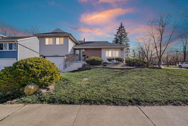 tri-level home with a garage, brick siding, and a lawn