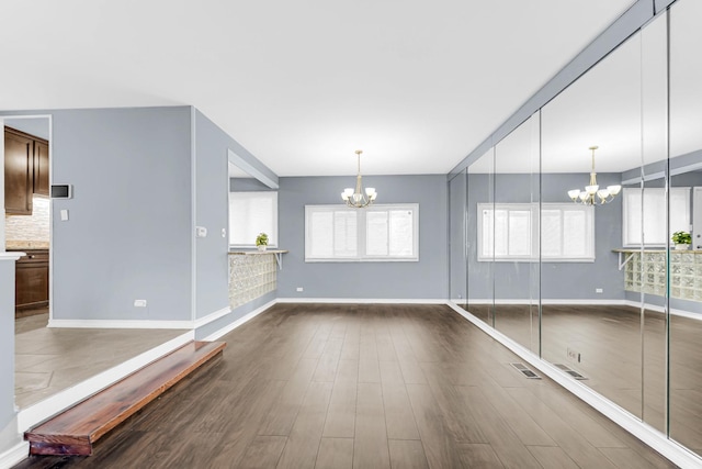 empty room featuring a chandelier, dark wood finished floors, visible vents, and baseboards