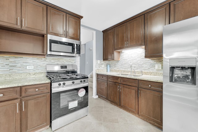 kitchen featuring light tile patterned floors, stainless steel appliances, a sink, light stone countertops, and tasteful backsplash