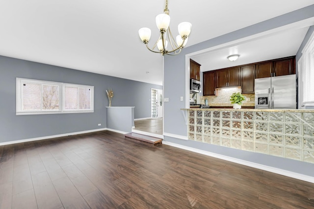 kitchen featuring dark wood-style floors, stainless steel appliances, backsplash, an inviting chandelier, and baseboards