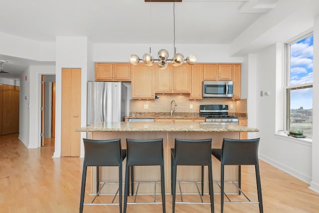 kitchen with stainless steel appliances, light wood-style floors, a sink, and tasteful backsplash