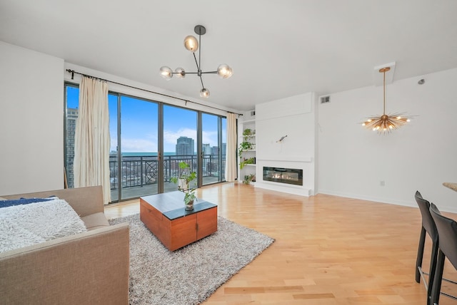 living area featuring light wood-style flooring, visible vents, baseboards, a glass covered fireplace, and an inviting chandelier