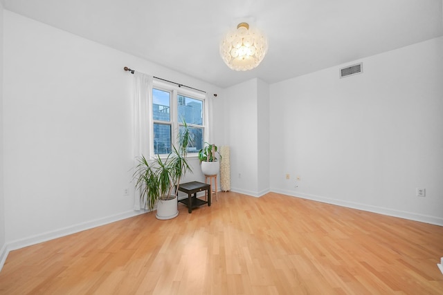 unfurnished room featuring light wood-type flooring, visible vents, baseboards, and an inviting chandelier