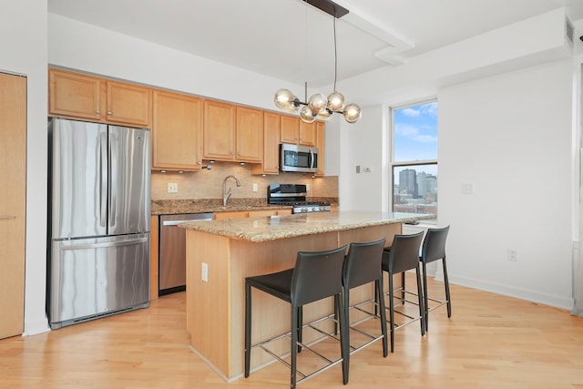 kitchen featuring tasteful backsplash, appliances with stainless steel finishes, a center island, light wood-type flooring, and a sink