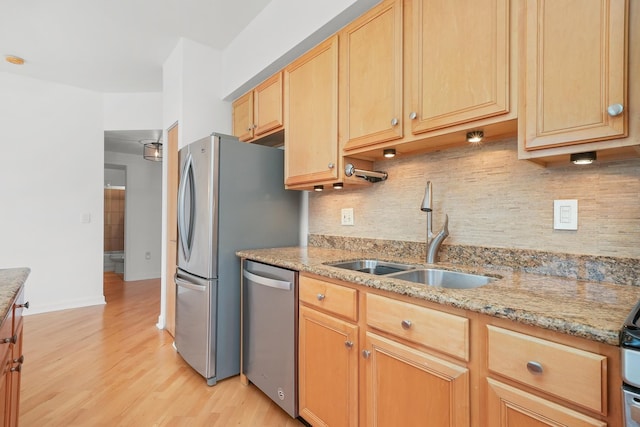 kitchen featuring stainless steel appliances, light wood finished floors, a sink, and light stone countertops