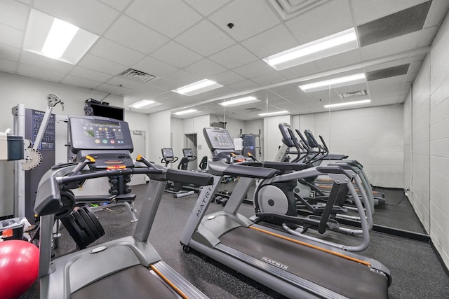 exercise room featuring a drop ceiling, visible vents, and concrete block wall