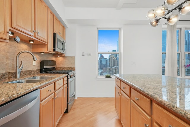 kitchen with decorative backsplash, light stone countertops, stainless steel appliances, light wood-type flooring, and a sink