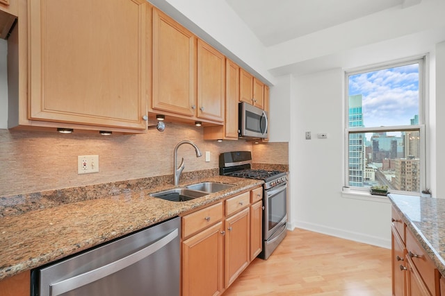 kitchen featuring stainless steel appliances, a sink, light wood-type flooring, backsplash, and light stone countertops