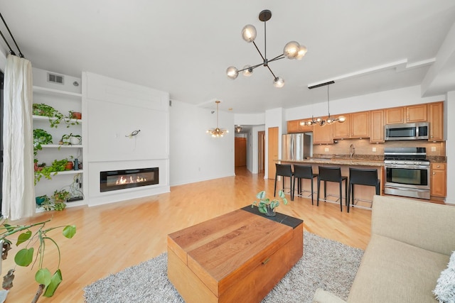 living area featuring light wood-type flooring, an inviting chandelier, visible vents, and a glass covered fireplace