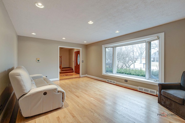 sitting room with visible vents, stairway, baseboards, and wood finished floors