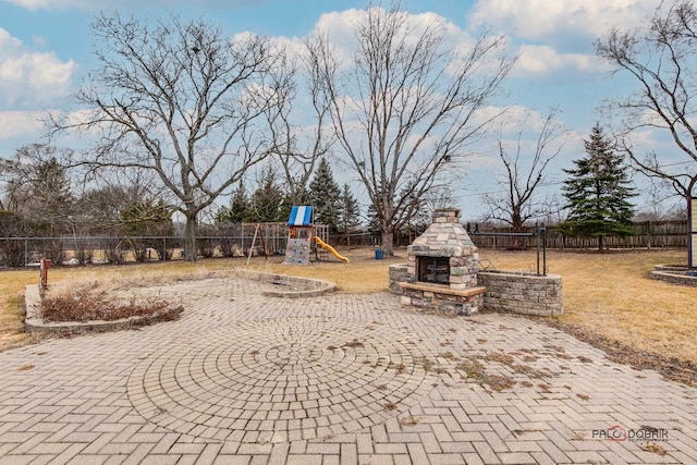 view of playground with a yard, an outdoor stone fireplace, fence, and a patio