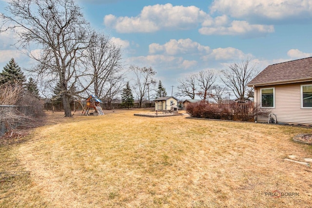 view of yard with a playground, an outdoor structure, a deck, and fence