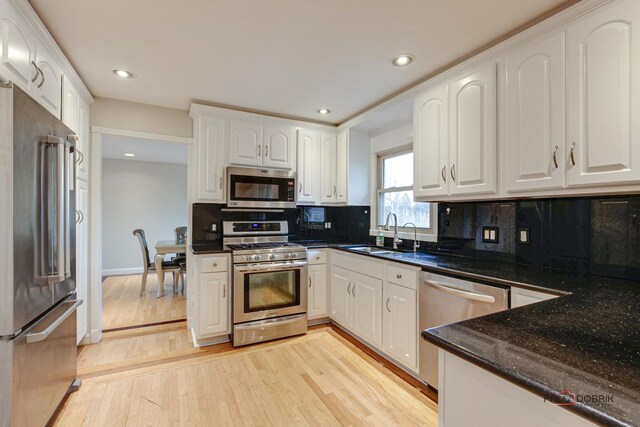 kitchen featuring light wood finished floors, tasteful backsplash, white cabinets, appliances with stainless steel finishes, and a sink