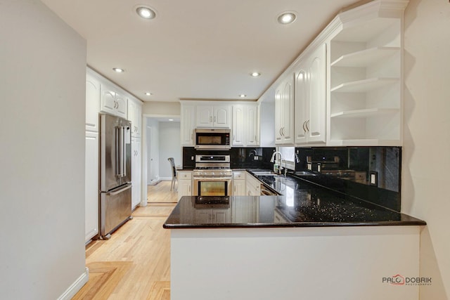 kitchen featuring stainless steel appliances, a peninsula, a sink, white cabinets, and open shelves