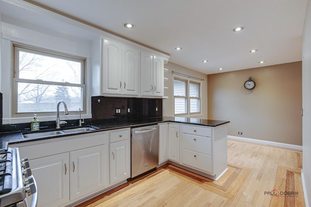 kitchen with a peninsula, stainless steel appliances, light wood-type flooring, white cabinetry, and a sink