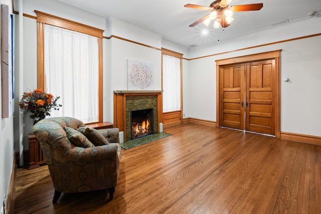 living room featuring a ceiling fan, a stone fireplace, baseboards, and wood finished floors