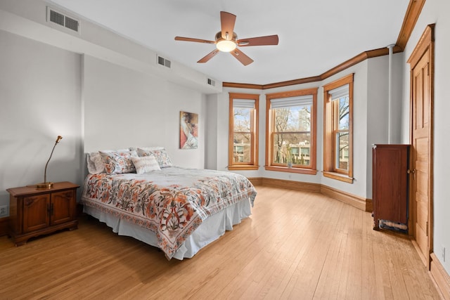 bedroom with light wood finished floors, baseboards, visible vents, and crown molding