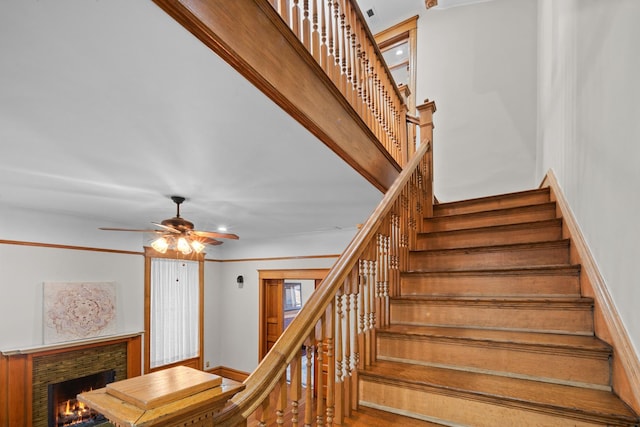 stairway with ceiling fan and a stone fireplace