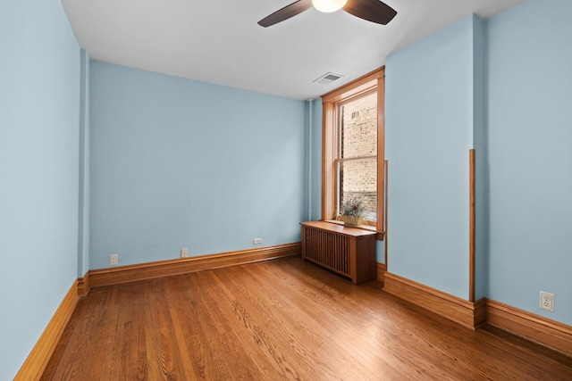 empty room with baseboards, visible vents, radiator heating unit, and wood finished floors