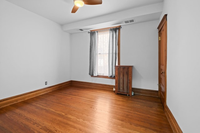 unfurnished room with radiator, visible vents, baseboards, and wood finished floors