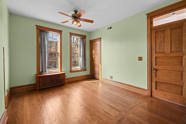 spare room featuring light wood-style flooring, radiator heating unit, visible vents, and baseboards