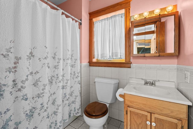 bathroom with toilet, a wainscoted wall, tile patterned flooring, vanity, and tile walls