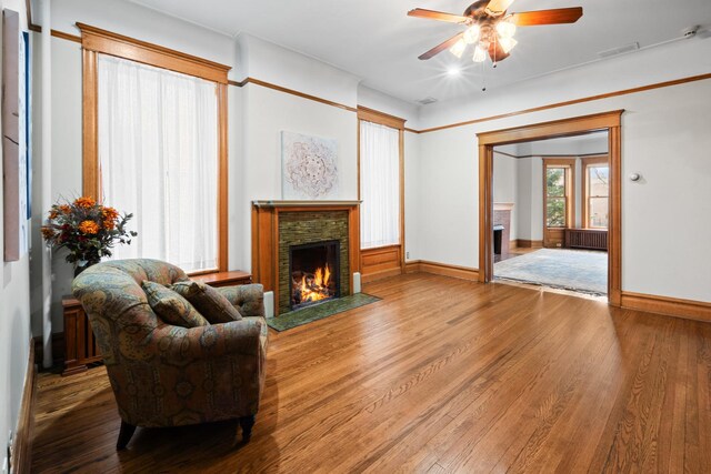 living room with radiator, baseboards, wood finished floors, and a stone fireplace