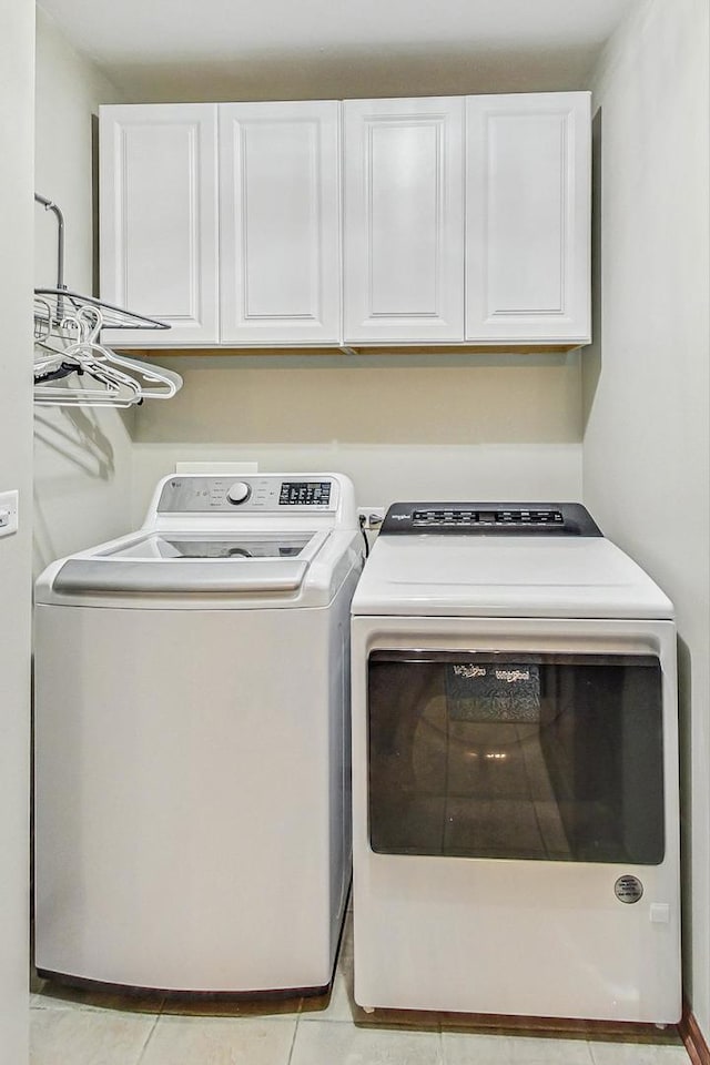 laundry area with washing machine and dryer, light tile patterned floors, and cabinet space