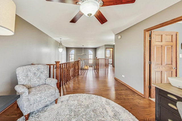 sitting room featuring an upstairs landing, wood finished floors, baseboards, and ceiling fan