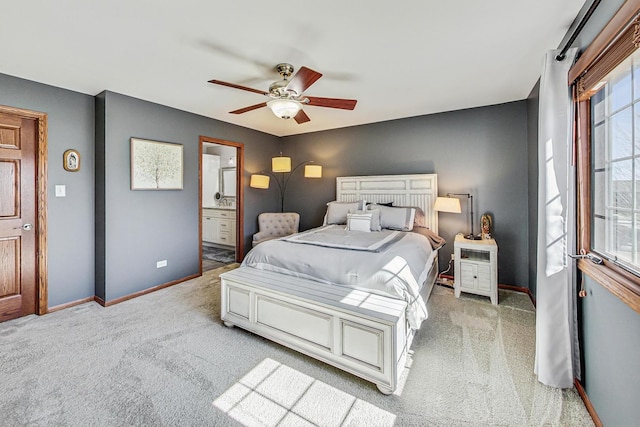 bedroom featuring baseboards, light colored carpet, ensuite bath, and a ceiling fan