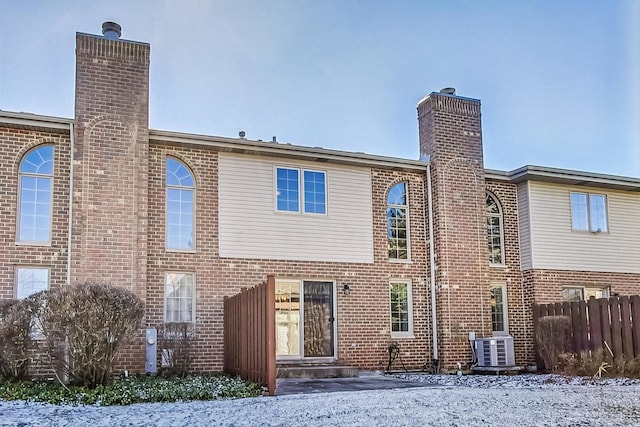 rear view of property with fence, brick siding, central AC, and a chimney