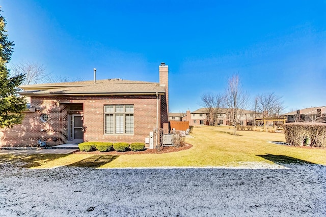 back of property featuring a yard, brick siding, and a chimney