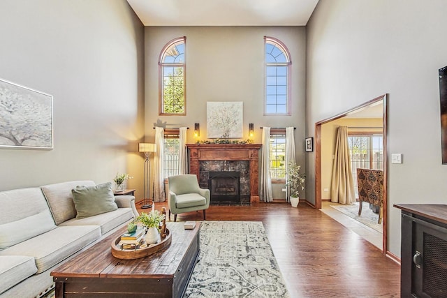 living area featuring a towering ceiling, baseboards, wood finished floors, and a high end fireplace