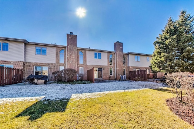 back of property featuring central air condition unit, a lawn, fence, brick siding, and a chimney