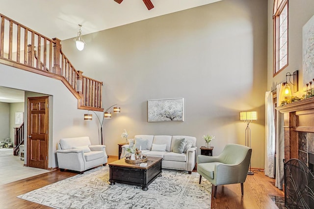 living room featuring wood finished floors, a ceiling fan, stairs, a towering ceiling, and a tiled fireplace