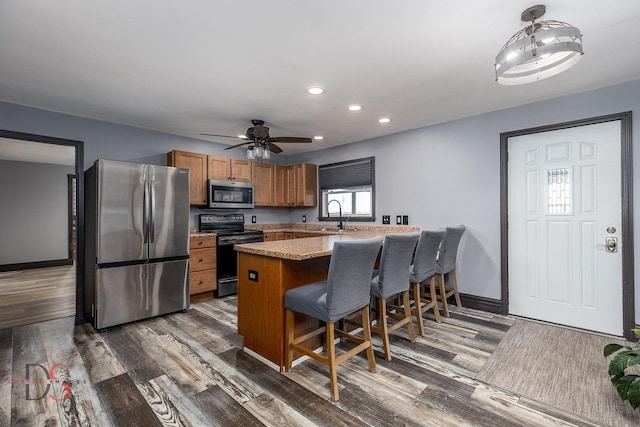 kitchen with stainless steel appliances, brown cabinetry, dark wood-type flooring, a peninsula, and a kitchen breakfast bar