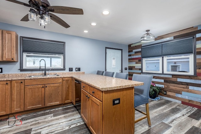 kitchen with a peninsula, a breakfast bar, a sink, light wood-style floors, and brown cabinetry