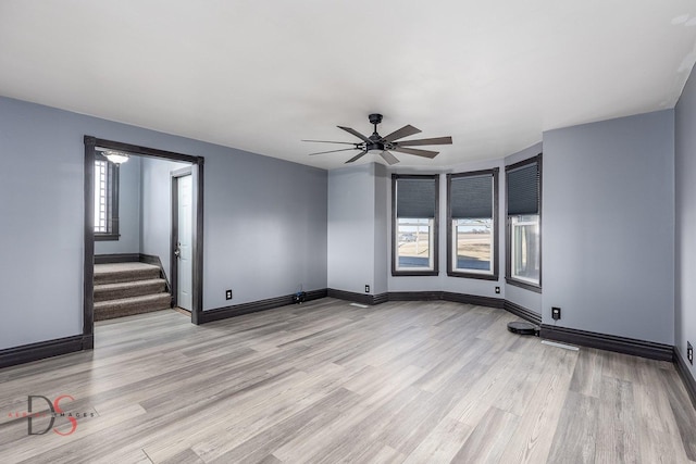 unfurnished room with a ceiling fan, baseboards, stairway, and light wood finished floors