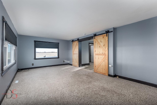 empty room with light carpet, a barn door, and baseboards