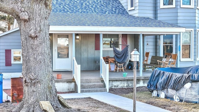 doorway to property featuring covered porch and roof with shingles