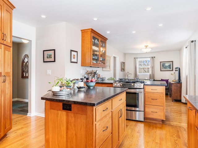 kitchen with light wood-type flooring, dark countertops, stainless steel gas stove, and glass insert cabinets