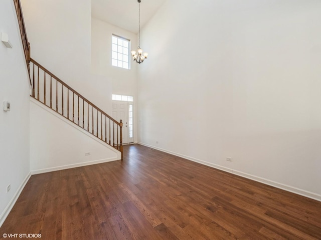 foyer entrance with baseboards, dark wood finished floors, stairway, an inviting chandelier, and a towering ceiling